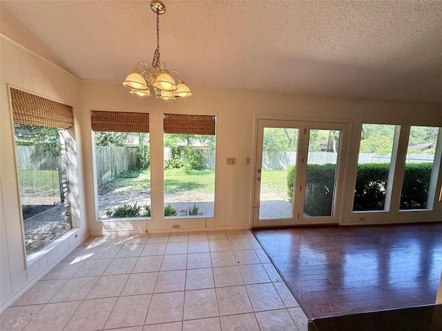 doorway with lofted ceiling, a textured ceiling, a chandelier, and light tile patterned floors