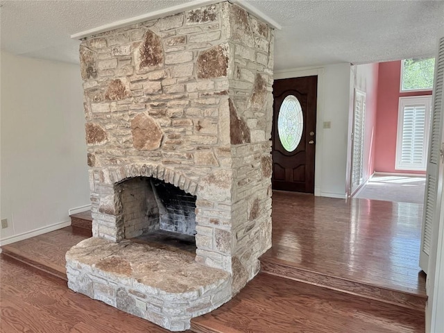 foyer entrance with a stone fireplace, baseboards, wood finished floors, and a textured ceiling