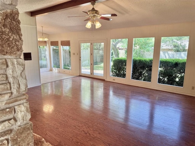 unfurnished living room featuring wooden walls, wood finished floors, beam ceiling, a textured ceiling, and ceiling fan with notable chandelier