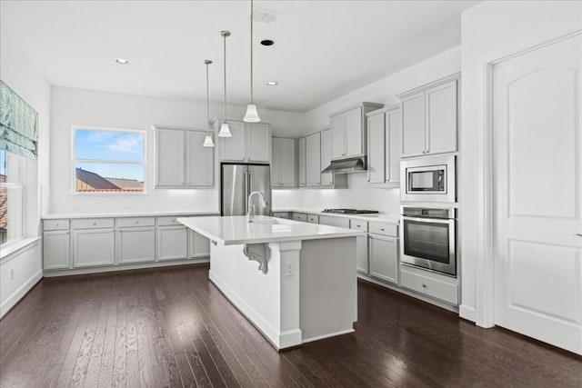 kitchen with a breakfast bar, stainless steel appliances, a kitchen island with sink, decorative light fixtures, and dark hardwood / wood-style floors