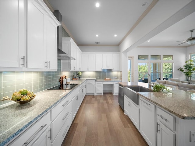 kitchen featuring sink, black electric cooktop, white cabinetry, and wall chimney range hood