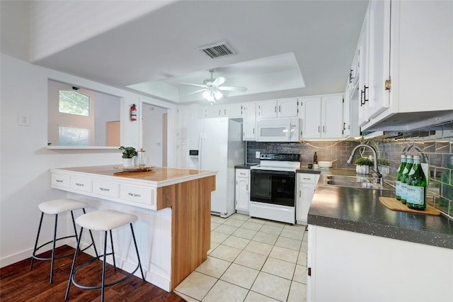 kitchen featuring white appliances, white cabinets, a kitchen breakfast bar, sink, and a tray ceiling