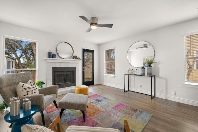 living room with dark wood-type flooring, a brick fireplace, ceiling fan, and a healthy amount of sunlight