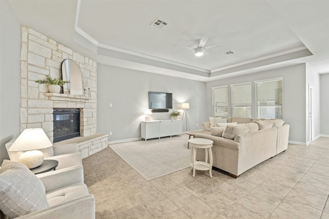 living room with ceiling fan, a raised ceiling, crown molding, a fireplace, and light tile patterned floors