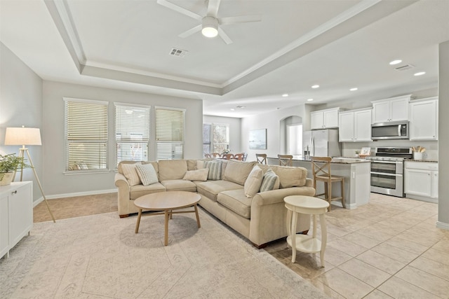 living room featuring a raised ceiling, ceiling fan, crown molding, and light tile patterned flooring