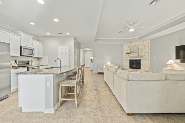 kitchen with appliances with stainless steel finishes, a raised ceiling, sink, a center island with sink, and white cabinets