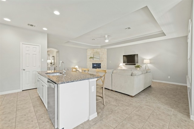 kitchen with white cabinetry, sink, ceiling fan, an island with sink, and a tray ceiling