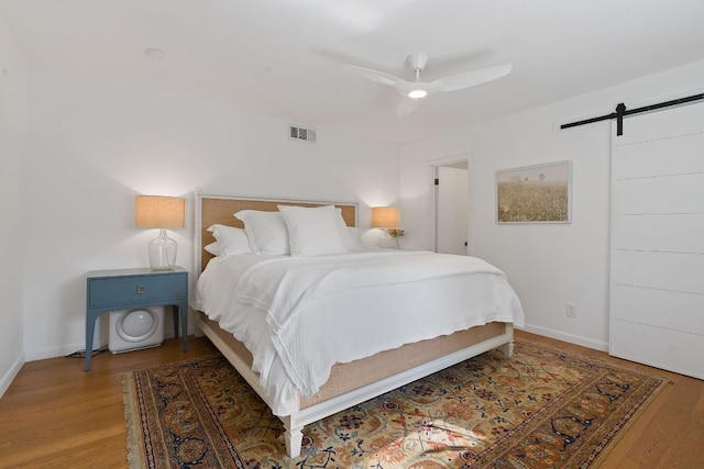 bedroom featuring hardwood / wood-style flooring, ceiling fan, and a barn door