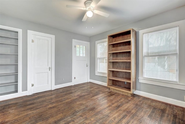 interior space featuring built in shelves, a healthy amount of sunlight, ceiling fan, and dark wood-type flooring