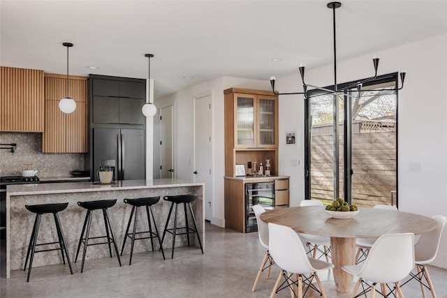 kitchen with a kitchen breakfast bar, hanging light fixtures, wine cooler, decorative backsplash, and appliances with stainless steel finishes