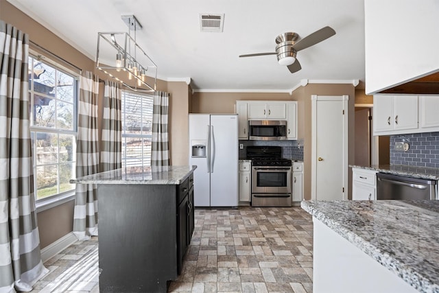 kitchen featuring appliances with stainless steel finishes, pendant lighting, a kitchen island, white cabinets, and tasteful backsplash