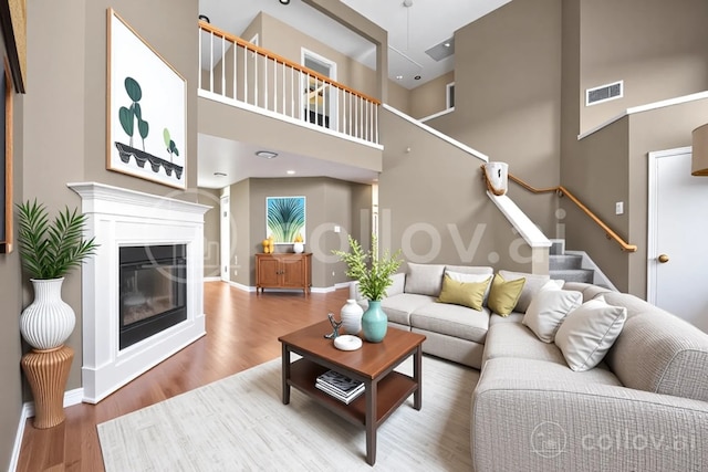 living room with visible vents, a glass covered fireplace, wood finished floors, baseboards, and stairway