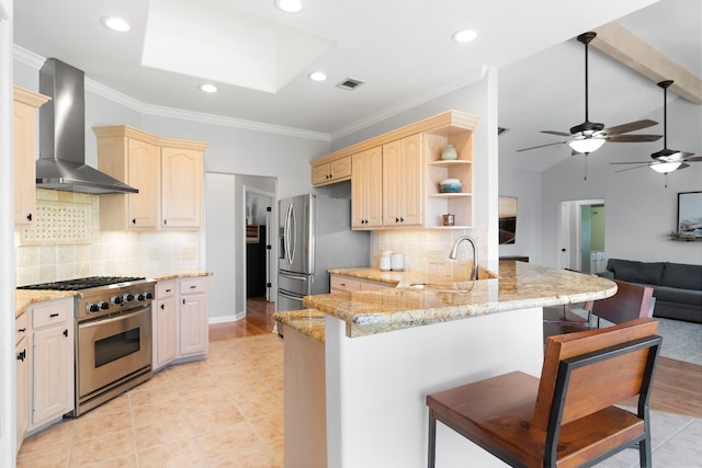 kitchen with stainless steel appliances, a peninsula, a sink, wall chimney range hood, and a kitchen bar