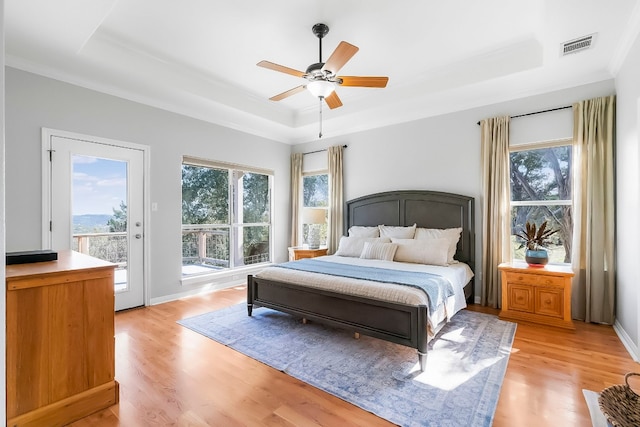 bedroom with ceiling fan, light hardwood / wood-style floors, access to outside, and a tray ceiling