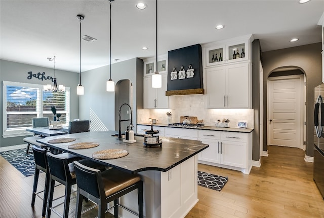 kitchen with white cabinetry, light hardwood / wood-style floors, decorative backsplash, decorative light fixtures, and a kitchen island with sink