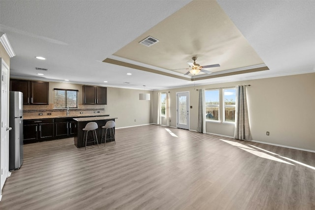 living room with a tray ceiling, crown molding, ceiling fan, and light wood-type flooring