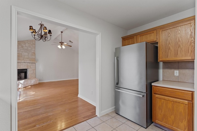 kitchen featuring light tile patterned floors, stainless steel fridge, a stone fireplace, tasteful backsplash, and ceiling fan with notable chandelier