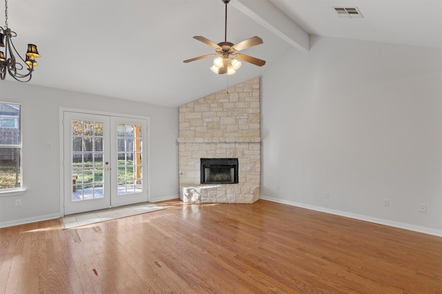 unfurnished living room with a fireplace, light hardwood / wood-style floors, lofted ceiling with beams, french doors, and ceiling fan with notable chandelier