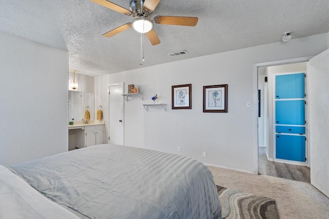 bedroom with carpet flooring, a textured ceiling, ensuite bathroom, and ceiling fan