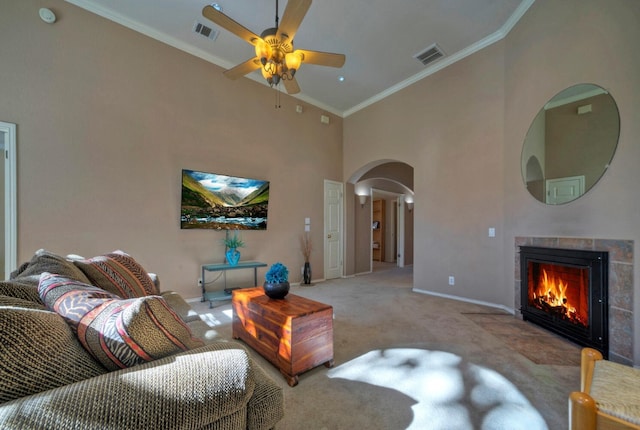 living room with light carpet, crown molding, ceiling fan, a towering ceiling, and a fireplace