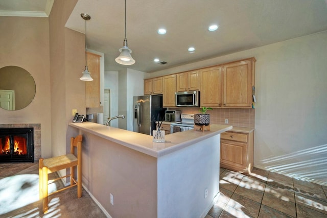 kitchen with stainless steel appliances, kitchen peninsula, decorative light fixtures, a tiled fireplace, and light brown cabinetry