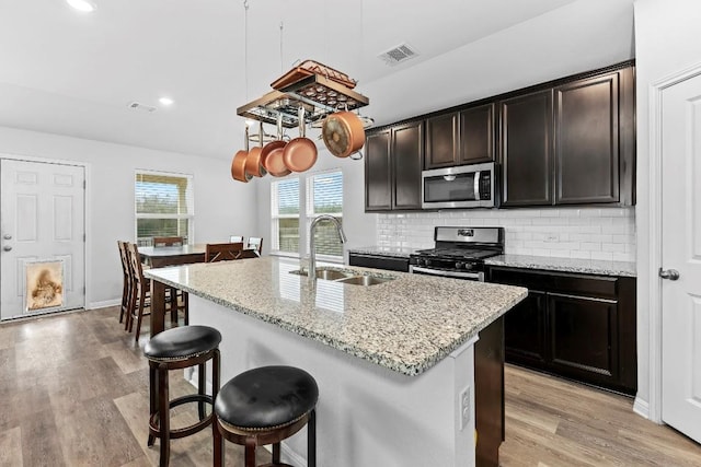 kitchen featuring backsplash, stainless steel appliances, a kitchen island with sink, sink, and light hardwood / wood-style flooring