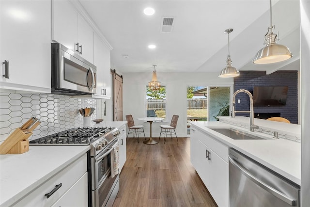 kitchen with white cabinetry, sink, stainless steel appliances, a barn door, and decorative light fixtures