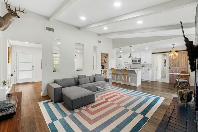 living room with vaulted ceiling with beams, a barn door, dark hardwood / wood-style floors, and sink