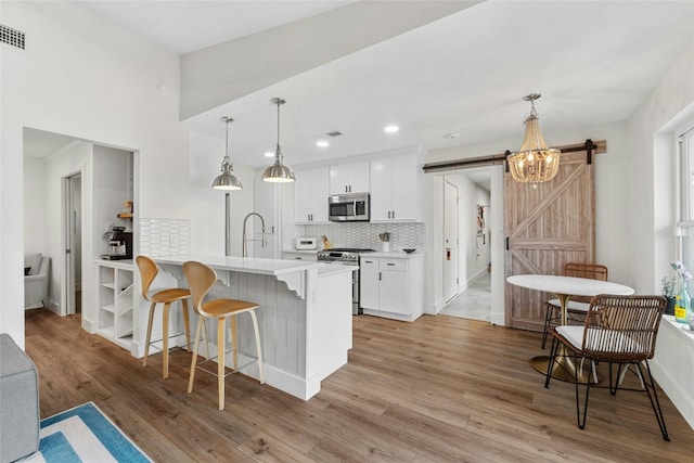 kitchen with light hardwood / wood-style flooring, a barn door, appliances with stainless steel finishes, decorative light fixtures, and white cabinetry