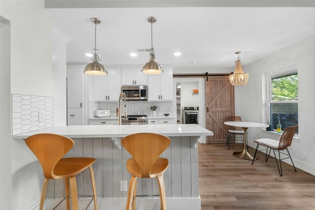 kitchen featuring hanging light fixtures, a barn door, backsplash, white cabinets, and appliances with stainless steel finishes