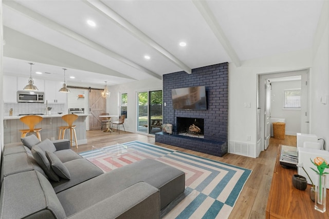 living room featuring lofted ceiling with beams, a barn door, light hardwood / wood-style floors, and a brick fireplace