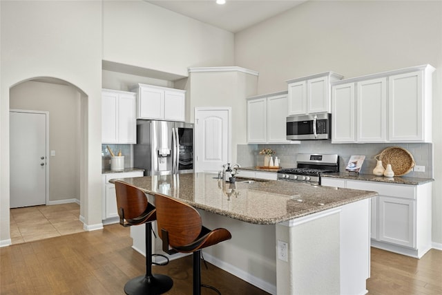 kitchen with white cabinetry, sink, a high ceiling, a center island with sink, and appliances with stainless steel finishes