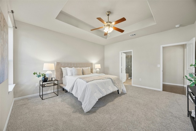 carpeted bedroom featuring ensuite bath, a raised ceiling, and ceiling fan