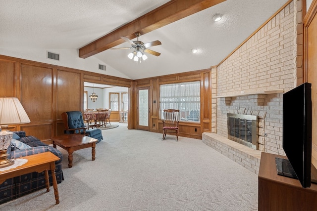 living room with carpet flooring, ceiling fan, a brick fireplace, lofted ceiling with beams, and a textured ceiling