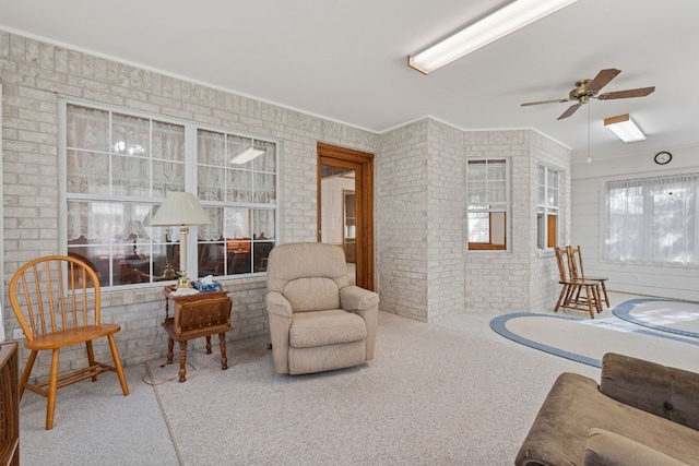 carpeted living room featuring ceiling fan, crown molding, and brick wall