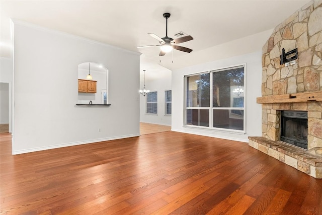 unfurnished living room with hardwood / wood-style flooring, ceiling fan with notable chandelier, a stone fireplace, and ornamental molding