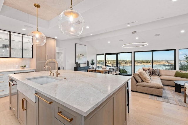 kitchen featuring sink, a kitchen island with sink, pendant lighting, light stone countertops, and light hardwood / wood-style floors