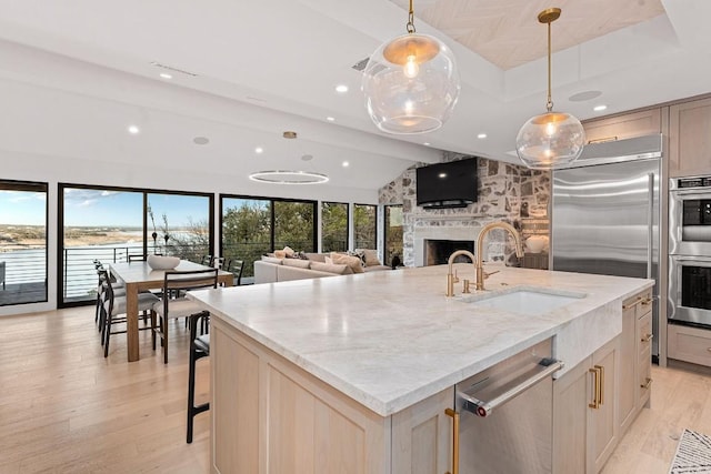 kitchen featuring a stone fireplace, pendant lighting, an island with sink, sink, and light stone counters