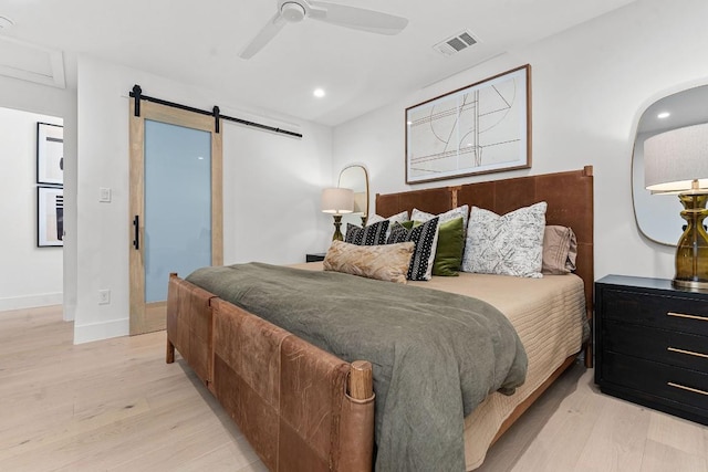 bedroom featuring a barn door, ceiling fan, and light wood-type flooring