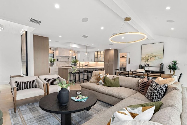 living room featuring sink, lofted ceiling with beams, and light wood-type flooring