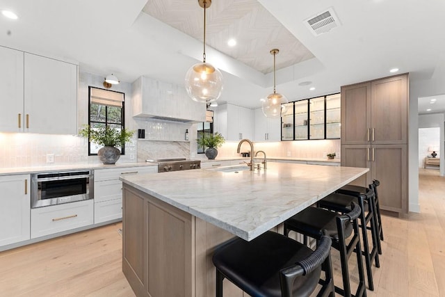 kitchen featuring pendant lighting, white cabinetry, a tray ceiling, a center island with sink, and light hardwood / wood-style flooring