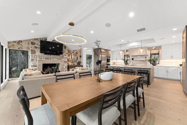 dining space featuring a stone fireplace, vaulted ceiling with beams, and light hardwood / wood-style floors