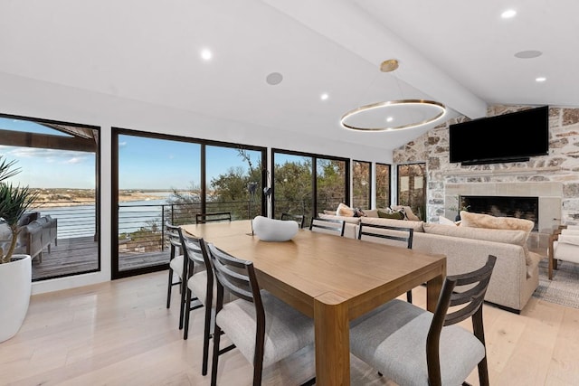 dining space featuring a water view, a stone fireplace, light hardwood / wood-style floors, and vaulted ceiling with beams