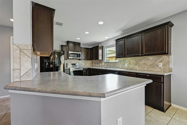 kitchen with dark brown cabinetry, decorative backsplash, light tile patterned floors, and stainless steel appliances