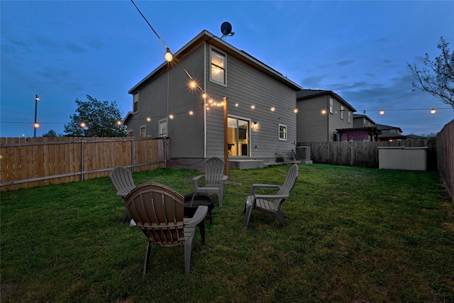 back house at dusk with a lawn and central AC unit