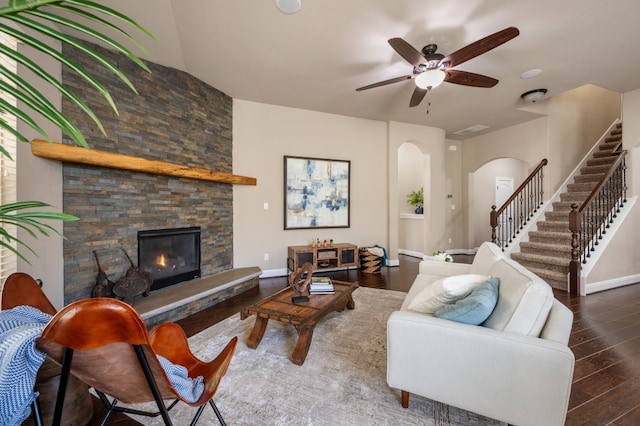 living room featuring a stone fireplace, ceiling fan, and dark wood-type flooring