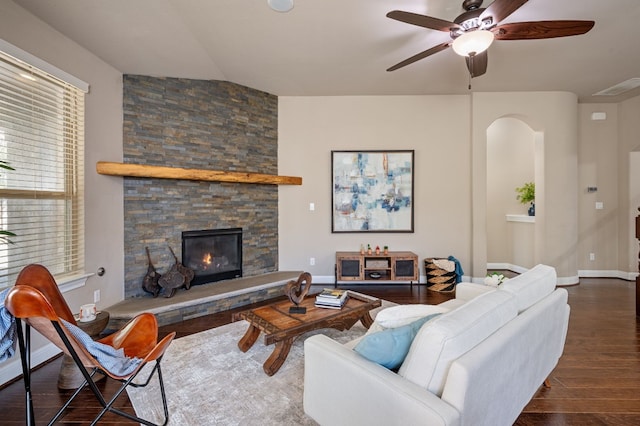 living room with lofted ceiling, a stone fireplace, ceiling fan, and dark wood-type flooring