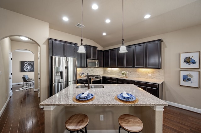 kitchen featuring light stone counters, stainless steel appliances, sink, decorative light fixtures, and a center island with sink