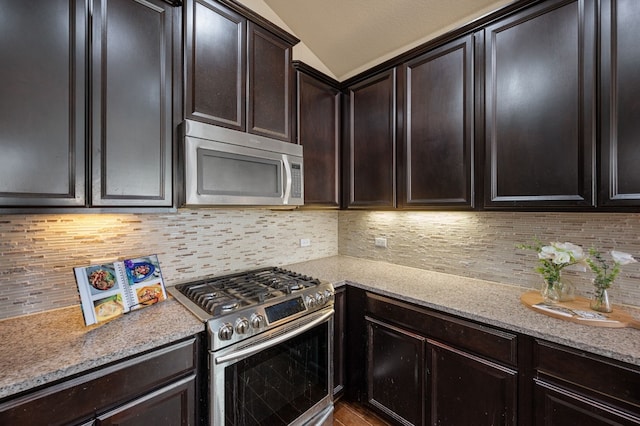 kitchen featuring light stone countertops, appliances with stainless steel finishes, tasteful backsplash, dark brown cabinets, and lofted ceiling