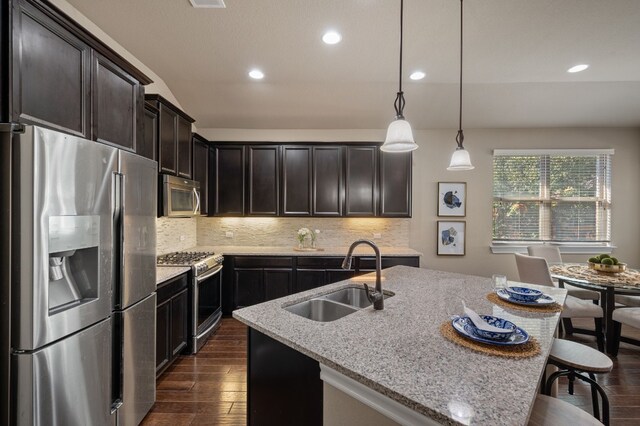 kitchen with a kitchen island with sink, sink, decorative light fixtures, light stone counters, and stainless steel appliances